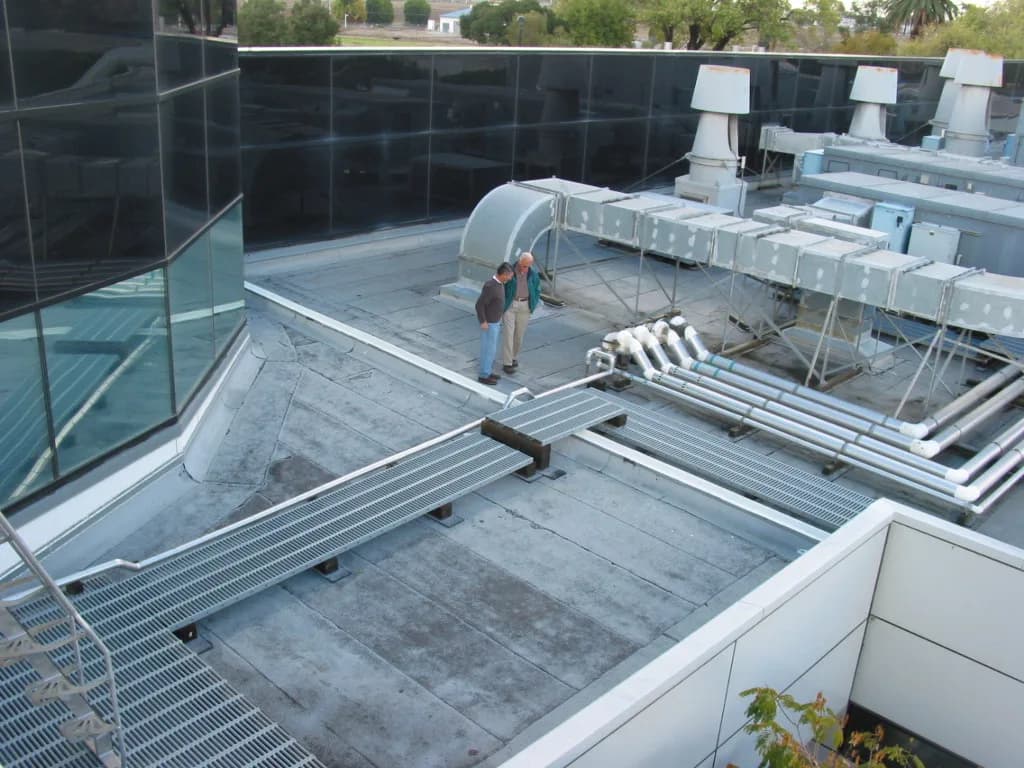 Two inspectors reviewing rooftop mechanical equipment and ductwork on a commercial building with dark glass curtain walls