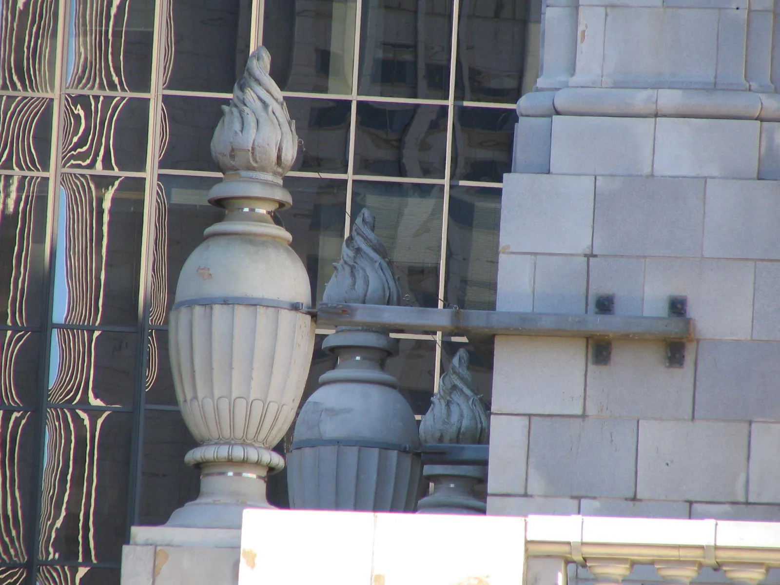 Carved stone ornament on a historic masonry parapet against a modern glass facade